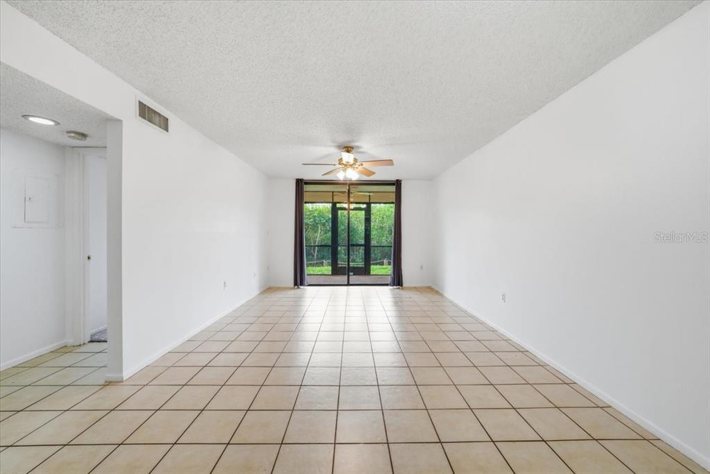 An empty living room features white walls, beige tile flooring, and a sliding glass door — 1332 PASADENA UNIT 102, SOUTH PASADENA, FL