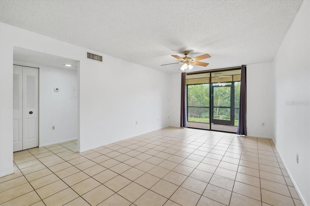 A living room with white walls, tile flooring, a ceiling fan, and a sliding glass door — 1332 PASADENA UNIT 102, SOUTH PASADENA, FL