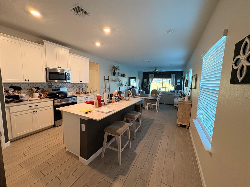 A kitchen with white cabinets, a central island with bar stools, and an open floor plan — 1525 NW 44TH COURT ROAD, OCALA, FL