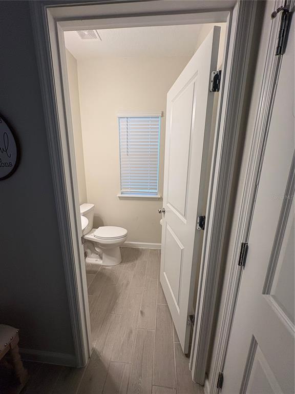 A small bathroom features light wood-look tile flooring, a white toilet, and a window with blinds — 1525 NW 44TH COURT ROAD, OCALA, FL