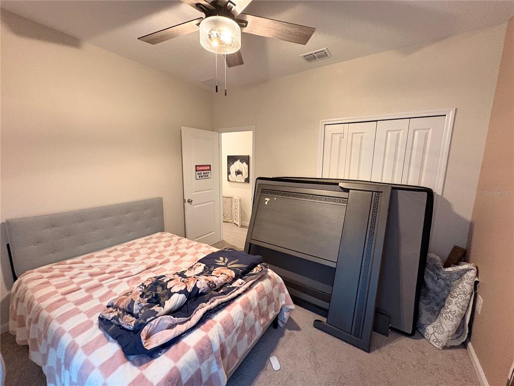 A bedroom features a bed with a patterned quilt, a ceiling fan, and stored furniture — 1525 NW 44TH COURT ROAD, OCALA, FL
