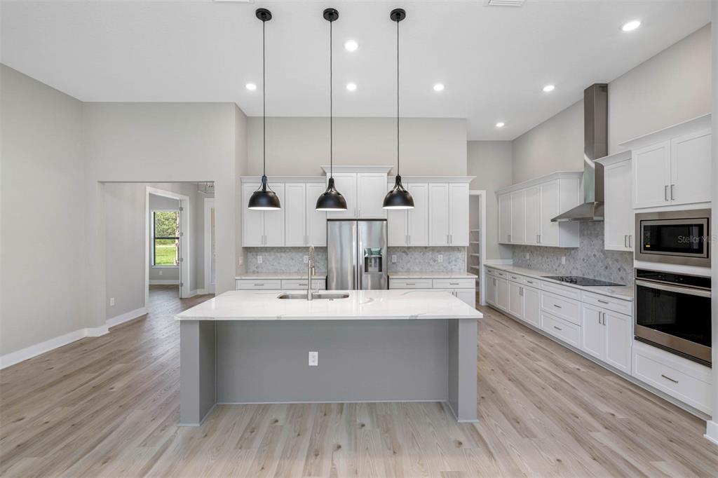 A modern kitchen features a gray island, white cabinetry, stainless steel appliances, and pendant lighting — 13704 OLDENBURG DRIVE, HUDSON, FL