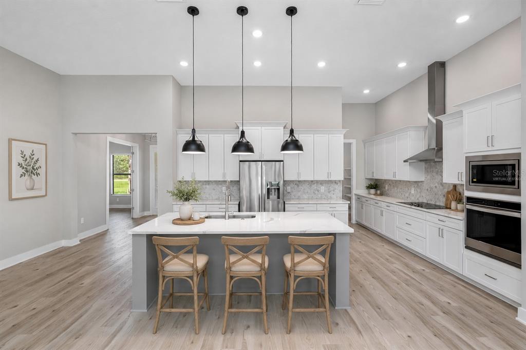 A modern kitchen features a central island with bar stools, white cabinetry, and stainless appliances — 13704 OLDENBURG DRIVE, HUDSON, FL