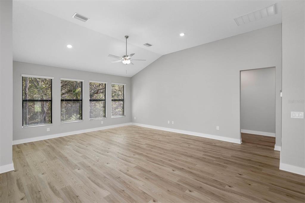 A spacious living room features light wood-look flooring, gray walls, and four large windows — 13704 OLDENBURG DRIVE, HUDSON, FL