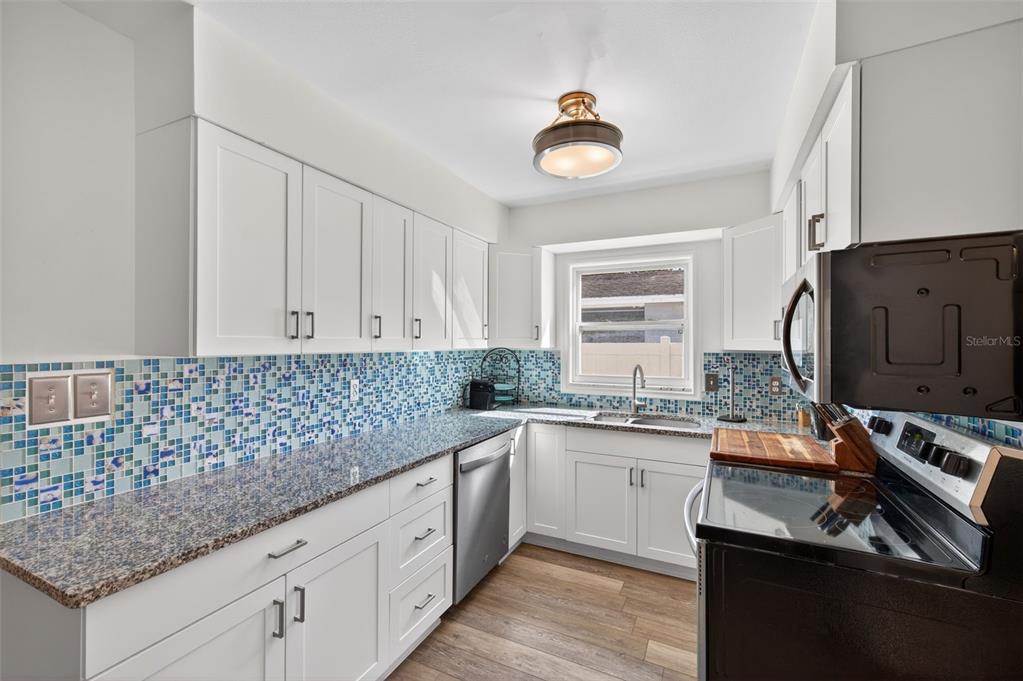 A kitchen with white cabinets, granite countertops, a blue mosaic backsplash, and stainless steel appliances — 5900 CYPRESS STREET N, ST PETERSBURG, FL