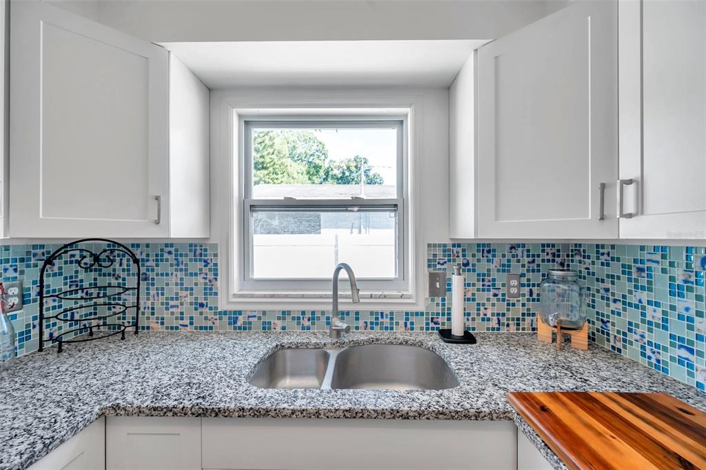 A kitchen sink area features granite countertops, blue mosaic tile backsplash, and white cabinets — 5900 CYPRESS STREET N, ST PETERSBURG, FL