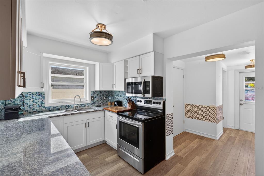 A kitchen with white cabinets, granite countertops, a mosaic tile backsplash, and stainless steel appliances — 5900 CYPRESS STREET N, ST PETERSBURG, FL