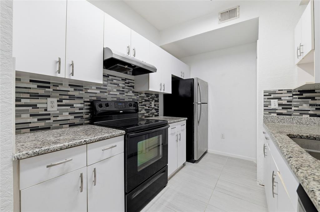 A kitchen features white cabinets, granite countertops, a black stove, and a mosaic tile backsplash — 17112 CARRINGTON PARK DRIVE UNIT 926, TAMPA, FL