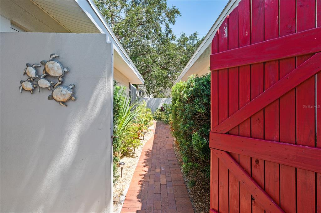 A brick walkway leads between a beige wall with turtle decor and a red gate — 6005 MIDNIGHT PASS ROAD UNIT S4, SARASOTA, FL