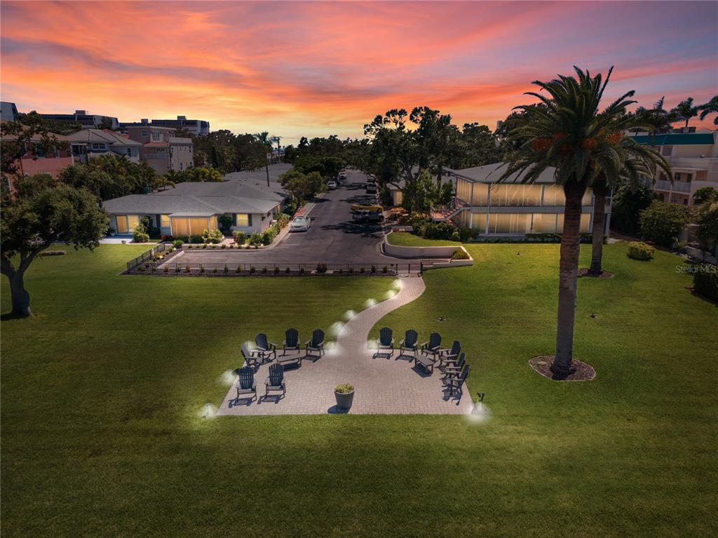 An aerial view of a grassy lawn with a paved patio, seating, and nearby buildings — 6005 MIDNIGHT PASS ROAD UNIT S4, SARASOTA, FL