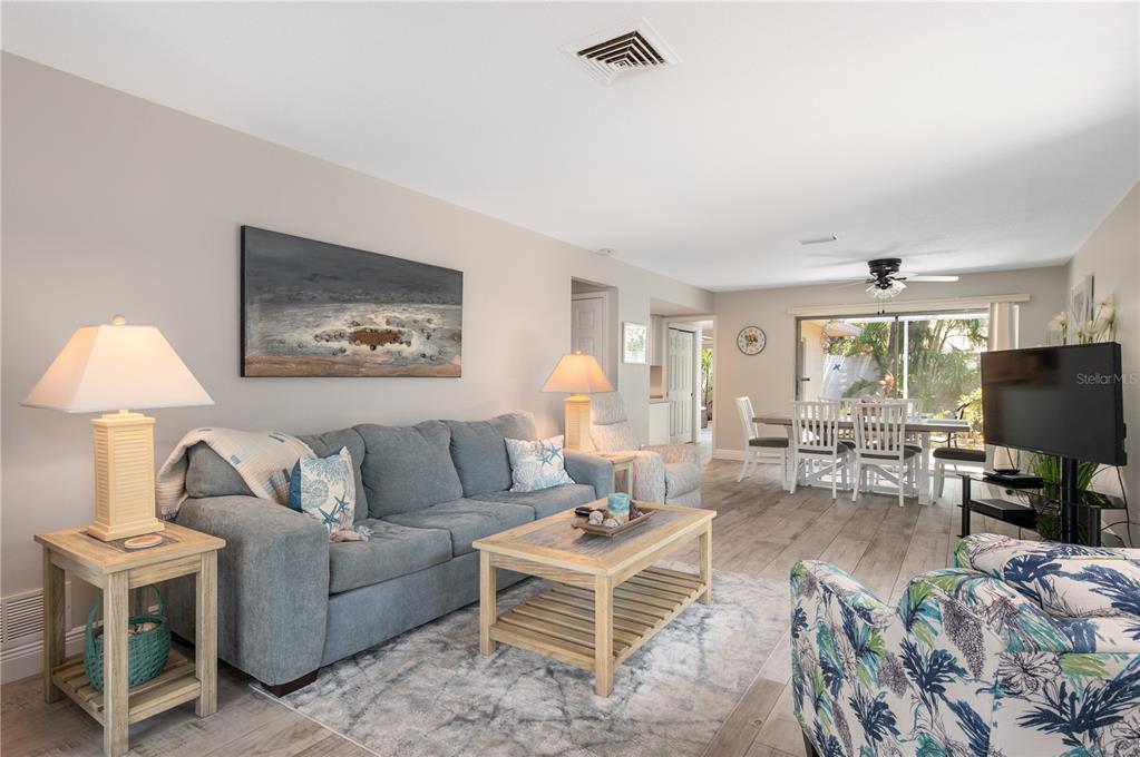 A living room with a blue sofa, patterned armchair, coffee table, and dining area beyond — 6005 MIDNIGHT PASS ROAD UNIT S4, SARASOTA, FL