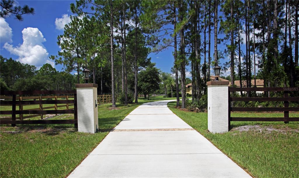 A concrete driveway leads through a gated entrance with white pillars and wooden fencing — 4345 OLD KINGS ROAD N, PALM COAST, FL