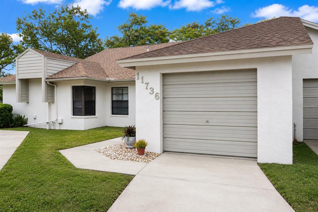 A single-story house with a white stucco exterior, a brown shingled roof, and a garage — 11736 ROLLING PINE LANE, PORT RICHEY, FL