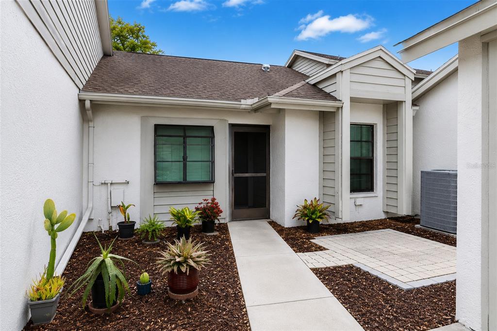 A concrete walkway leads to the front entrance of a house with a small patio — 11736 ROLLING PINE LANE, PORT RICHEY, FL