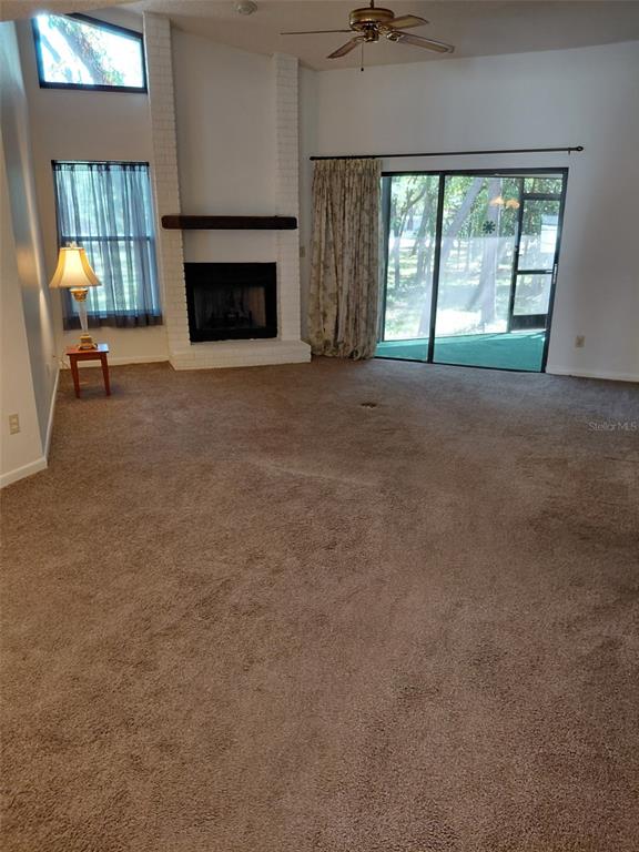 A living room features a white brick fireplace, carpeted flooring, and sliding glass patio doors — 11736 ROLLING PINE LANE, PORT RICHEY, FL