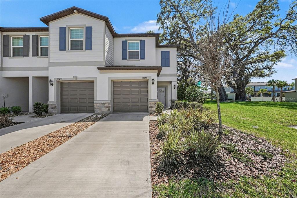 A two-story townhouse exterior features a concrete driveway, two garage doors, and a grassy yard — 36456 WELL HILL WAY, ZEPHYRHILLS, FL
