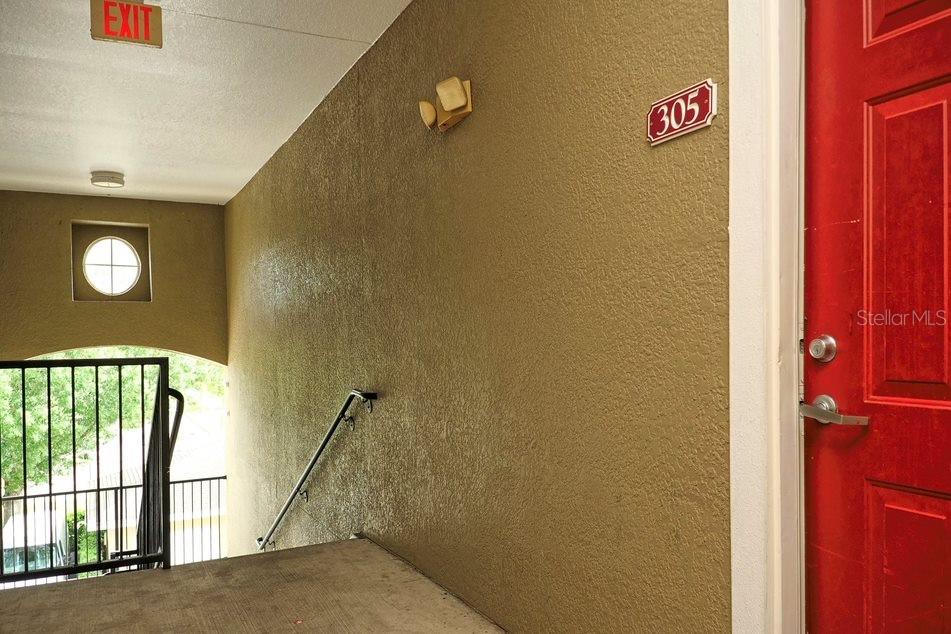A red apartment door labeled 305 is located next to an outdoor stairwell and exit sign — 8225 CLAIRE ANN DRIVE UNIT 305, ORLANDO, FL