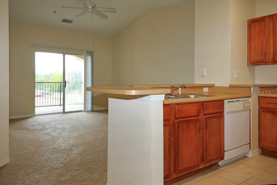 A kitchen with wood cabinets and a breakfast bar overlooks a carpeted living area — 8225 CLAIRE ANN DRIVE UNIT 305, ORLANDO, FL