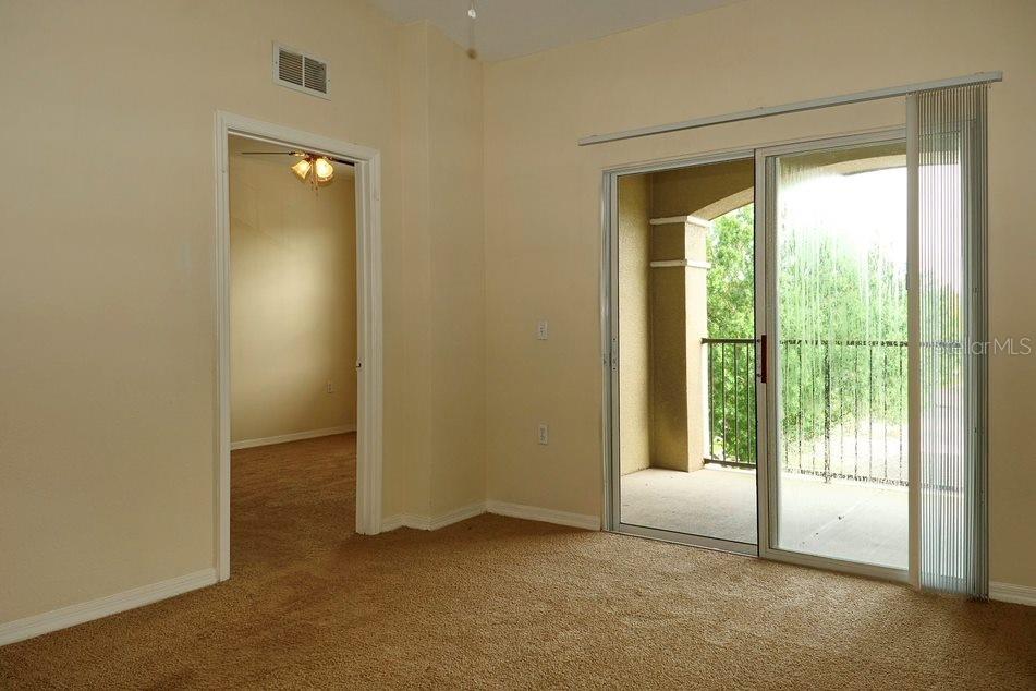 An empty bedroom features beige carpeting, tan walls, a doorway to another room, and sliding glass doors — 8225 CLAIRE ANN DRIVE UNIT 305, ORLANDO, FL