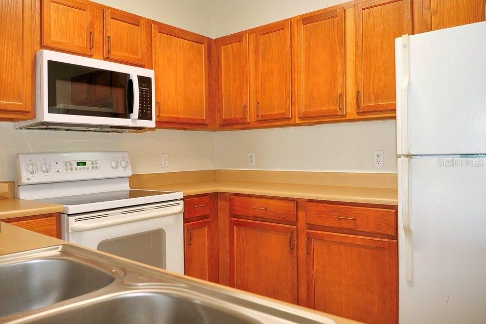 A kitchen features wooden cabinets, white appliances, and tan countertops — 8225 CLAIRE ANN DRIVE UNIT 305, ORLANDO, FL