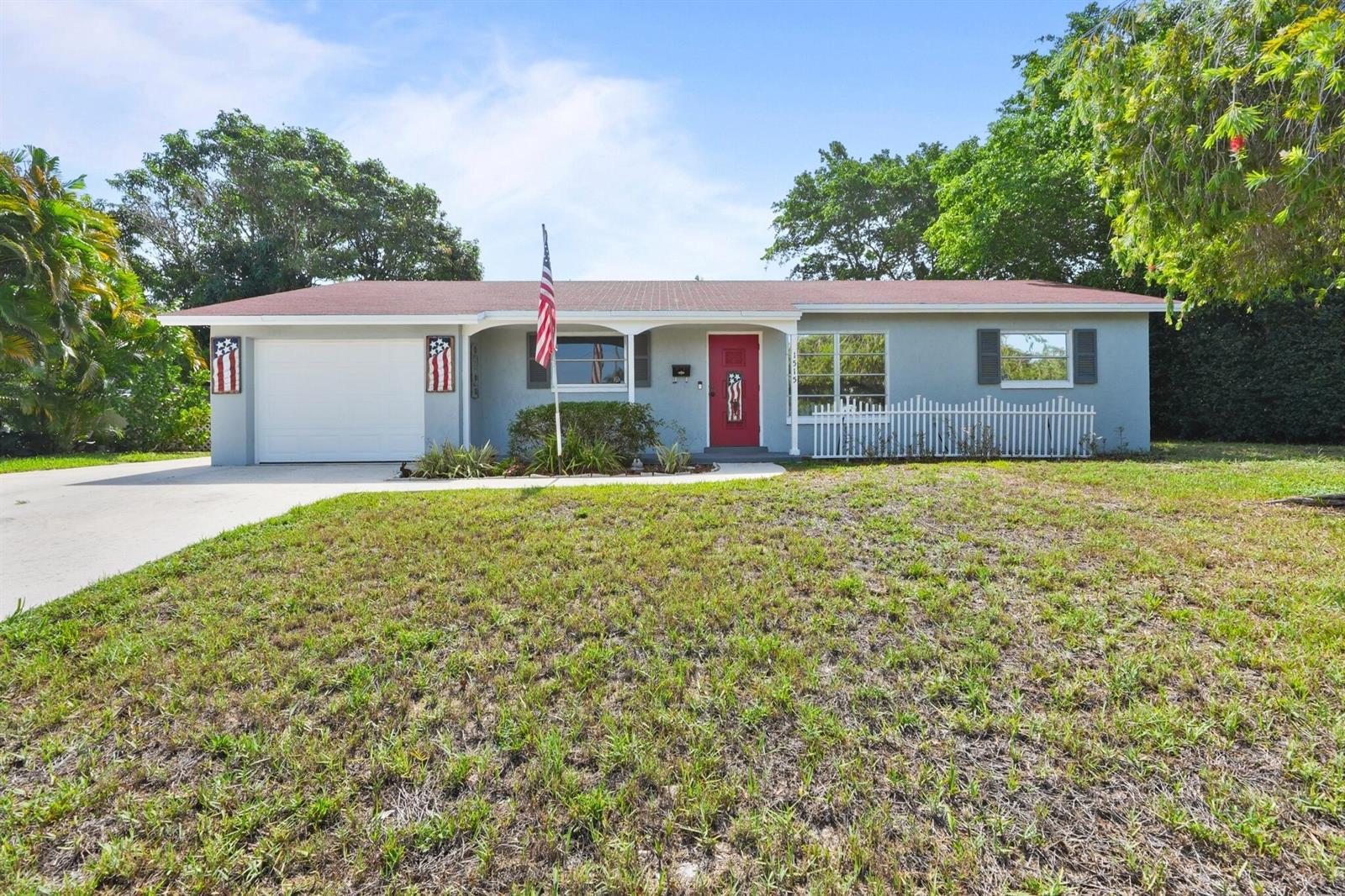 A single-story gray house features a red front door, a garage, and an American flag — 1515 CRESCENT Drive, Lake Park FL 33403, LAKE PARK, FL