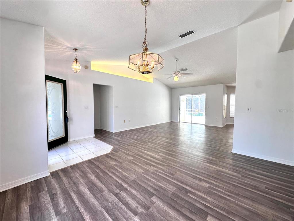 An open-concept living area features wood-look flooring, vaulted ceilings, and a decorative chandelier — 29439 SCHINNECOCK HILLS LANE, SAN ANTONIO, FL