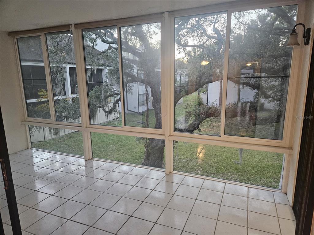 A sunroom with white tiled flooring and large windows overlooking a grassy yard and trees — 4723 PURITAN CIRCLE UNIT 624, TAMPA, FL