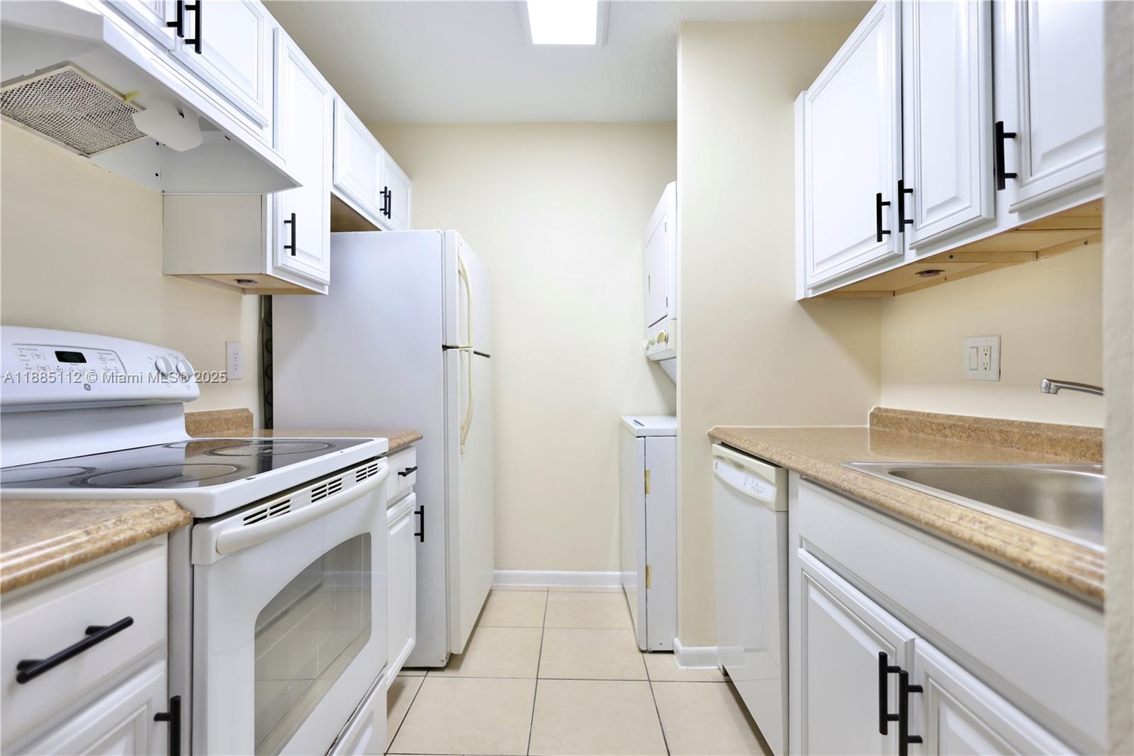 A galley kitchen features white cabinets, black hardware, tan countertops, and a stacked laundry unit — 10016 Twin Lakes Dr # C, Coral Springs FL 33071, CORAL SPRINGS, FL