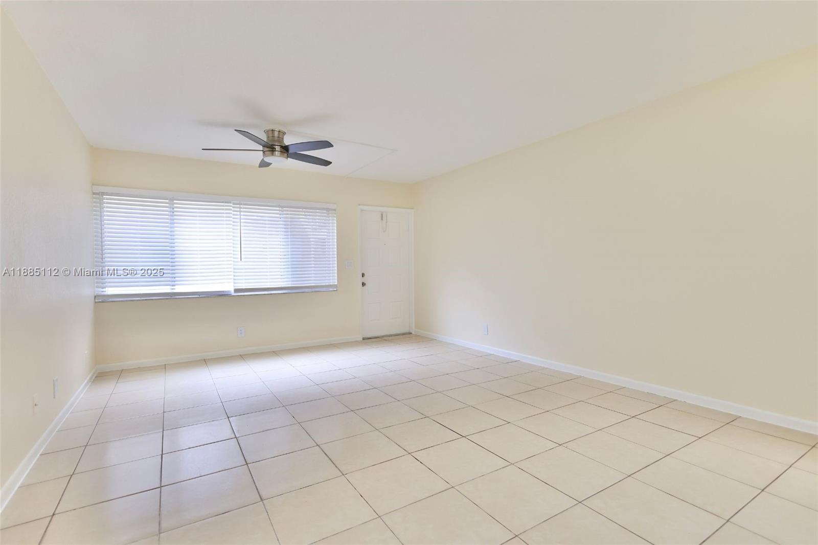 An empty room features beige tile flooring, light-colored walls, a ceiling fan, and window blinds — 10016 Twin Lakes Dr # C, Coral Springs FL 33071, CORAL SPRINGS, FL