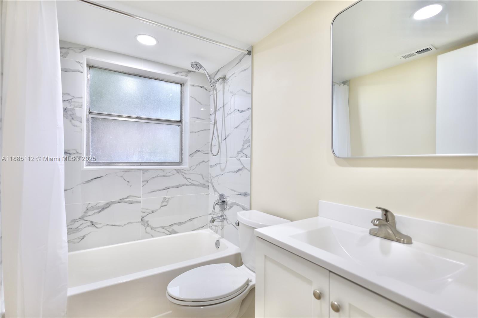 A bathroom features a white vanity, a toilet, and a bathtub with marble-patterned tile walls — 10016 Twin Lakes Dr # C, Coral Springs FL 33071, CORAL SPRINGS, FL