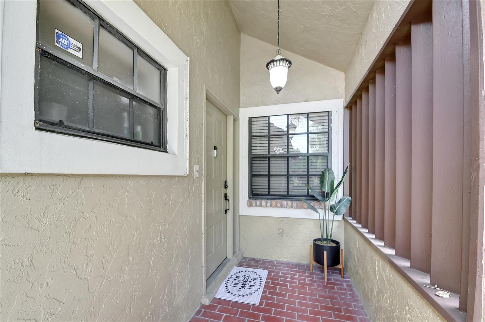 A covered entryway features a brick floor, a front door, two windows, and a potted plant — 8071 Popash Court, Boynton Beach FL 33472, BOYNTON BEACH, FL