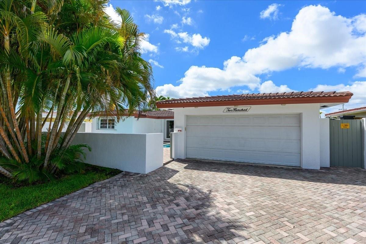 A paved driveway leads to a white house with a garage and a palm tree — 200 SE 11th Street, Pompano Beach FL 33060, POMPANO BEACH, FL