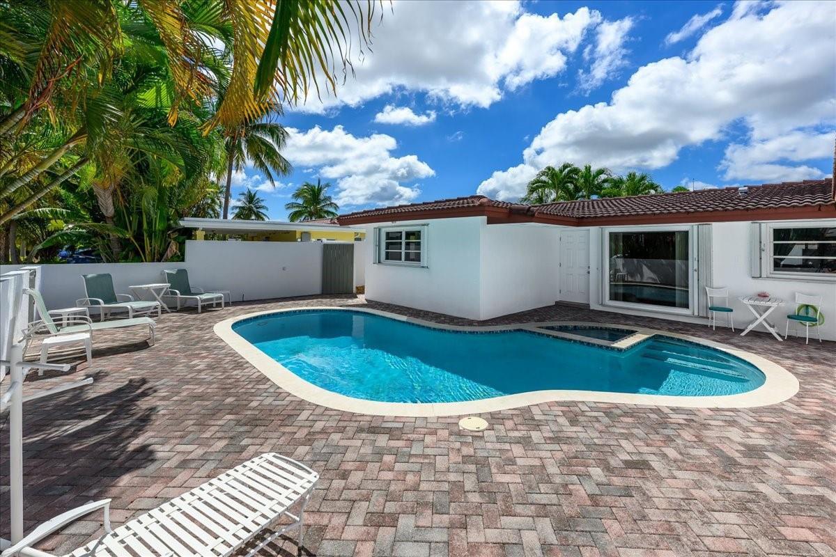A kidney-shaped swimming pool sits on a brick paver patio next to a white house — 200 SE 11th Street, Pompano Beach FL 33060, POMPANO BEACH, FL