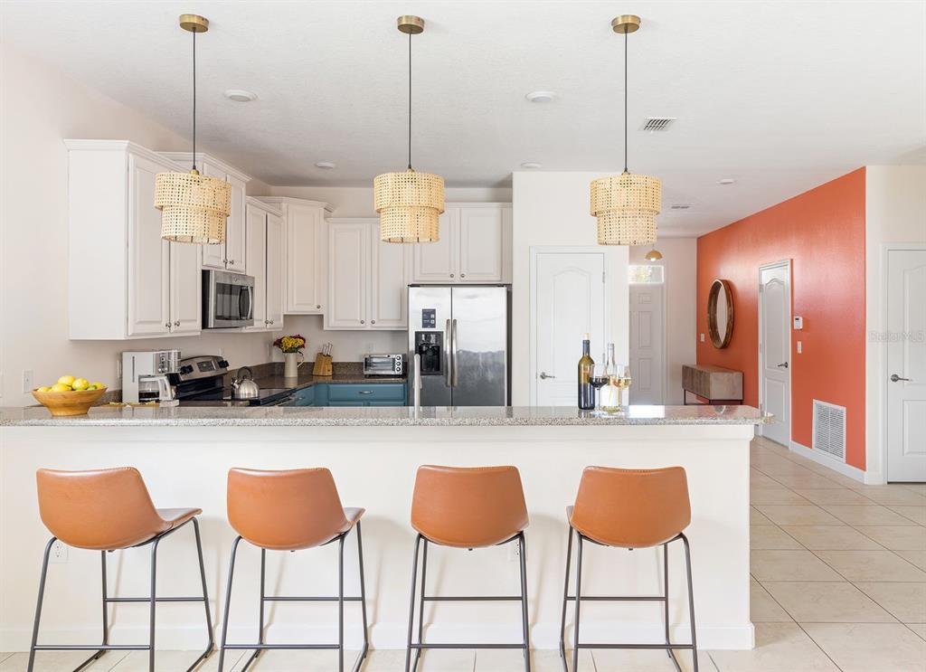 A kitchen with white cabinets, a granite breakfast bar, and three tan bar stools — 9034 SHADOW MOUNTAIN STREET, DAVENPORT, FL
