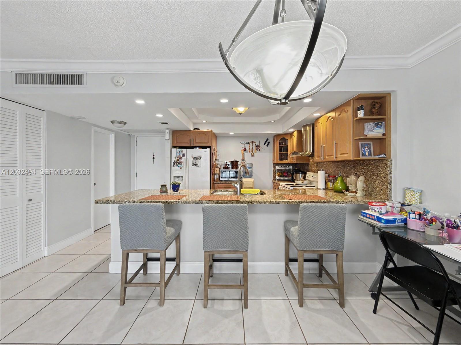 A kitchen features a granite breakfast bar with three gray stools and wooden cabinetry — 5701 Collins Ave # 1711, Miami Beach FL 33140, MIAMI BEACH, FL