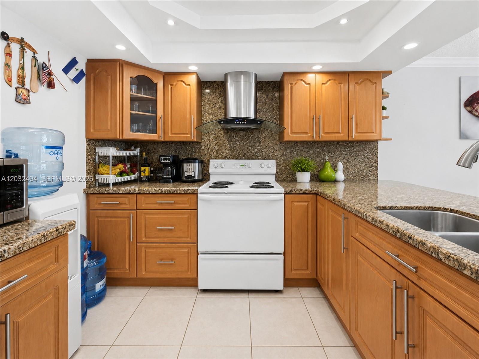 A kitchen features wood cabinets, granite countertops, a white stove, and a stainless steel hood — 5701 Collins Ave # 1711, Miami Beach FL 33140, MIAMI BEACH, FL
