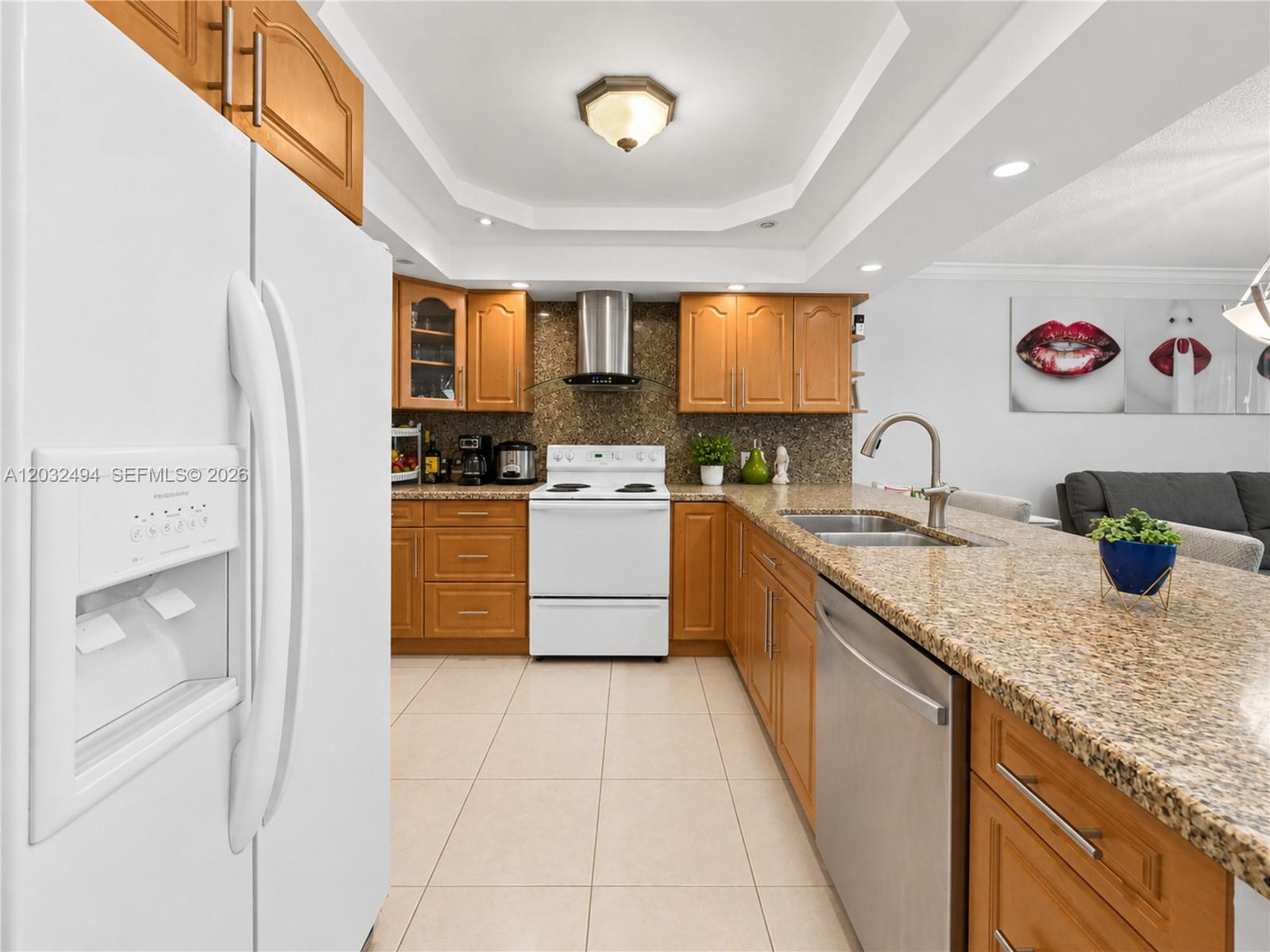 A kitchen features wood cabinets, granite countertops, stainless steel appliances, and a white refrigerator — 5701 Collins Ave # 1711, Miami Beach FL 33140, MIAMI BEACH, FL