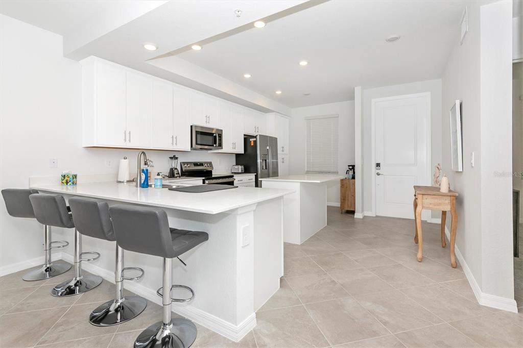 A modern kitchen features white cabinetry, quartz countertops, a breakfast bar, and gray bar stools — 17565 OPAL SAND DRIVE UNIT 305, VENICE, FL
