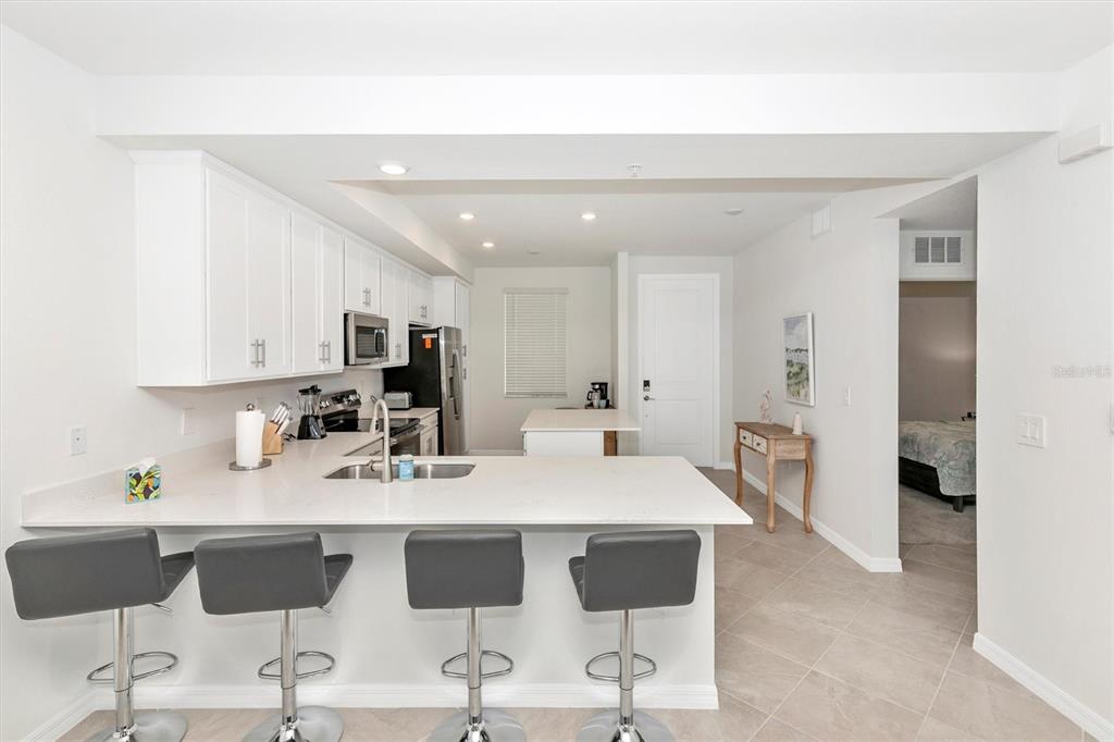 A kitchen with white cabinets, a quartz breakfast bar, and four grey bar stools — 17565 OPAL SAND DRIVE UNIT 305, VENICE, FL