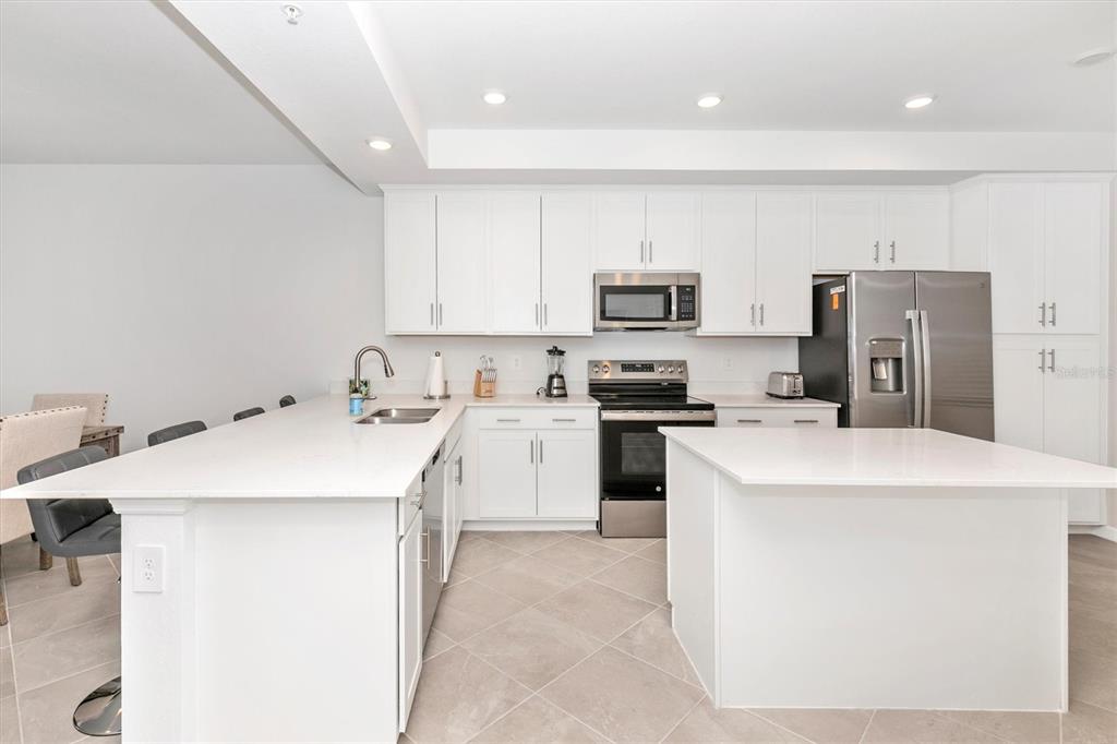 A modern kitchen features white cabinetry, stainless steel appliances, a large island, and tile flooring — 17565 OPAL SAND DRIVE UNIT 305, VENICE, FL