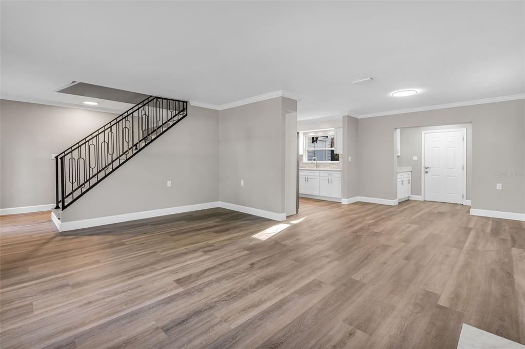 A living area with wood-look flooring, a black metal staircase railing, and an adjacent kitchen — 216 S SHORE CREST DRIVE, TAMPA, FL