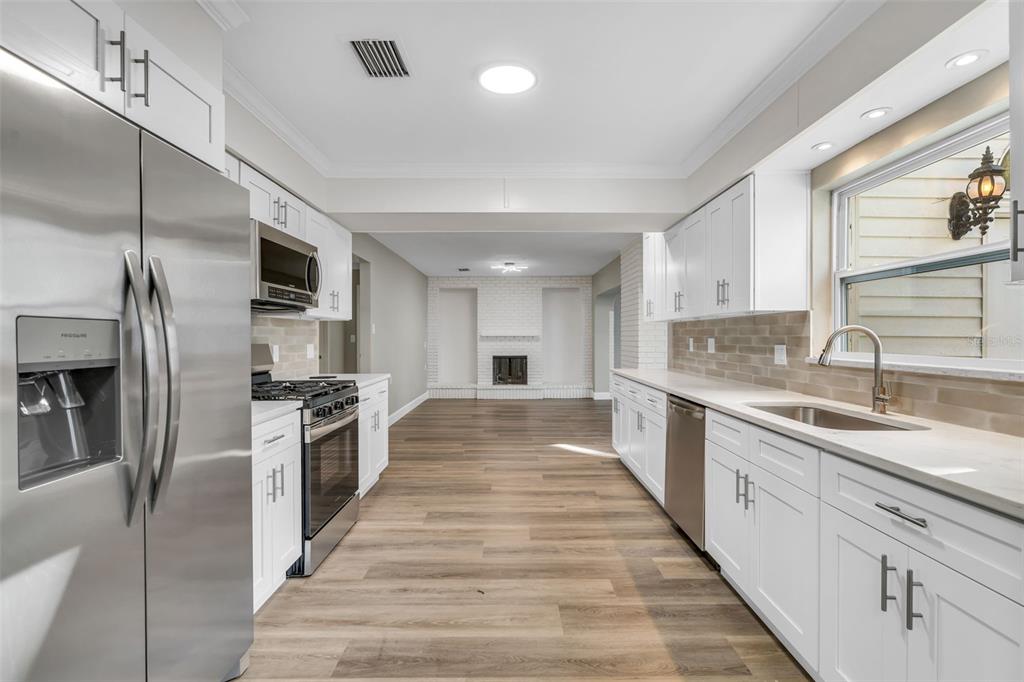 A kitchen with white cabinets, stainless steel appliances, and wood-look flooring leads to a living area — 216 S SHORE CREST DRIVE, TAMPA, FL