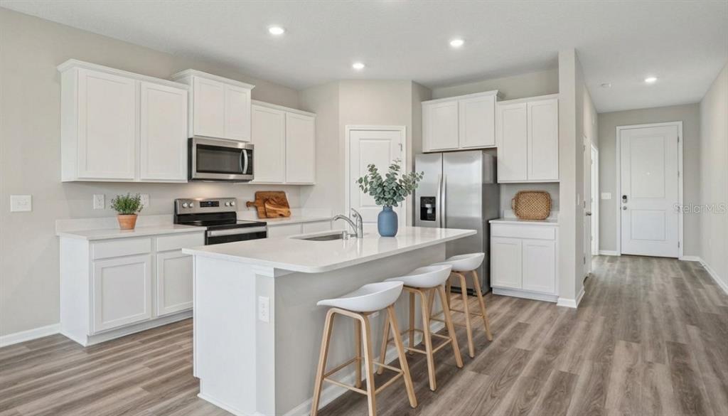 A modern kitchen features white cabinets, stainless steel appliances, a center island, and wood-look flooring — 32744 WEATHERED OAK DRIVE, WESLEY CHAPEL, FL
