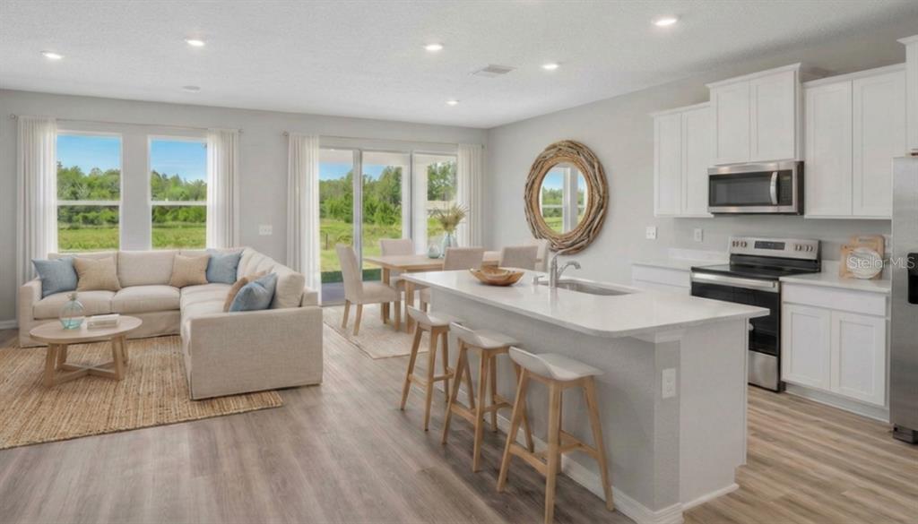 An open-concept kitchen and living area with white cabinetry, a center island, and neutral furniture — 32744 WEATHERED OAK DRIVE, WESLEY CHAPEL, FL