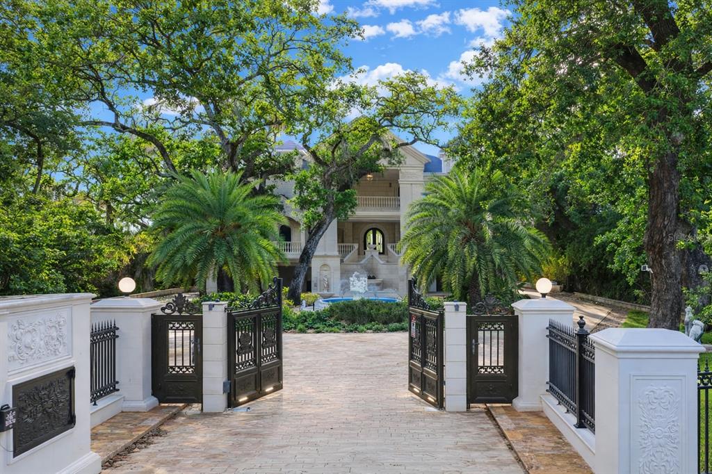 A gated driveway leads to a large multi-story mansion with a fountain and palm trees — 2000 PARK STREET N, ST PETERSBURG, FL