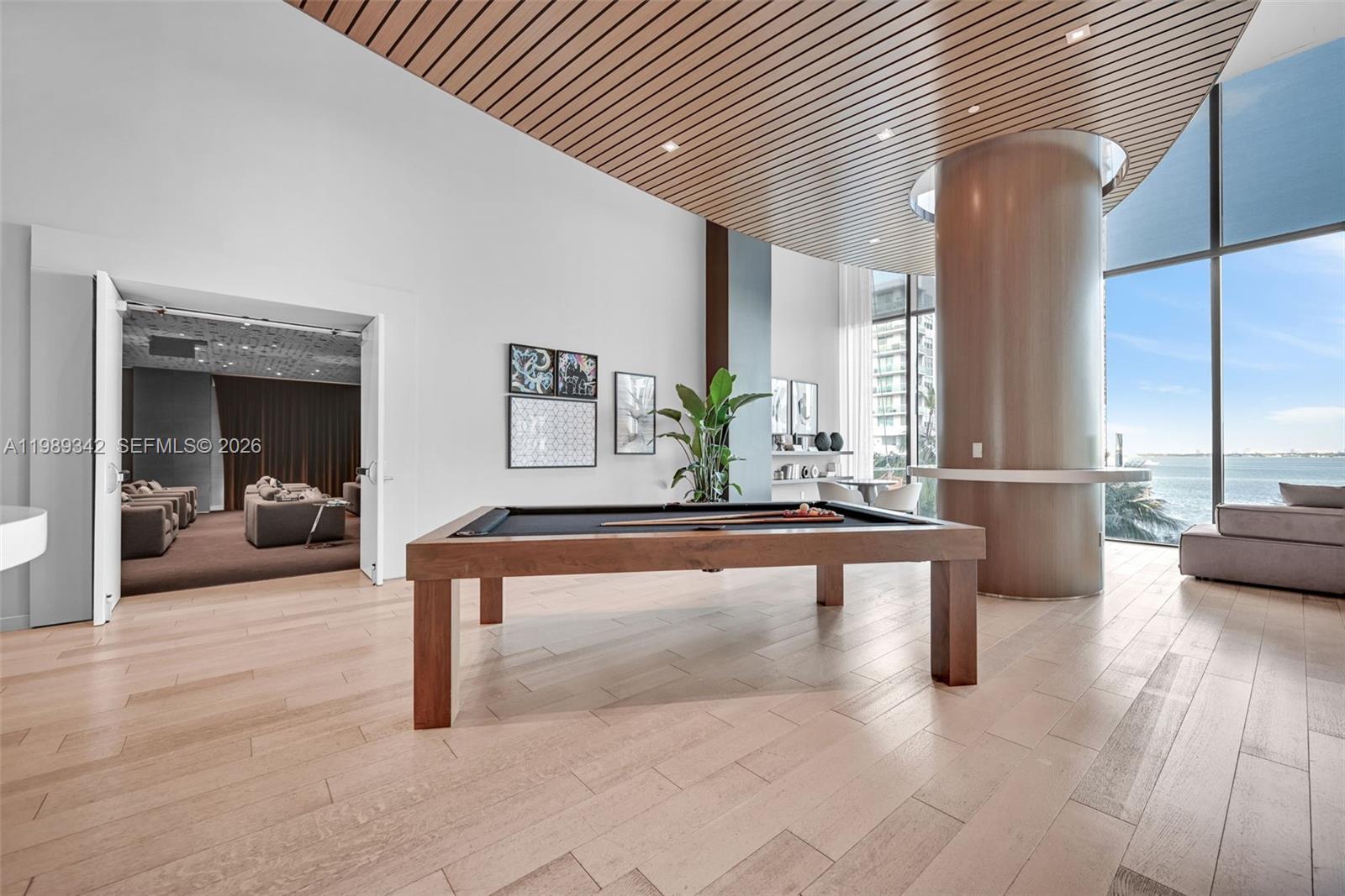 A modern game room features a pool table, wood-slat ceiling, and floor-to-ceiling windows with water views — 460 NE 28th St # 601, Miami FL 33137, MIAMI, FL