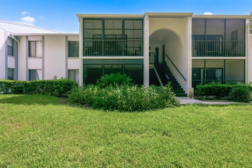 A two-story apartment building exterior featuring screened balconies, a central staircase, and landscaped grounds — 1204 PINE RIDGE CIRCLE W UNIT C1, TARPON SPRINGS, FL