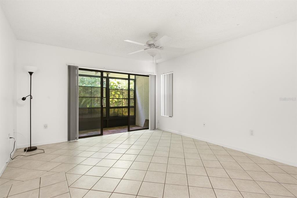 An empty living room features white walls, tile flooring, a ceiling fan, and sliding glass doors — 1204 PINE RIDGE CIRCLE W UNIT C1, TARPON SPRINGS, FL