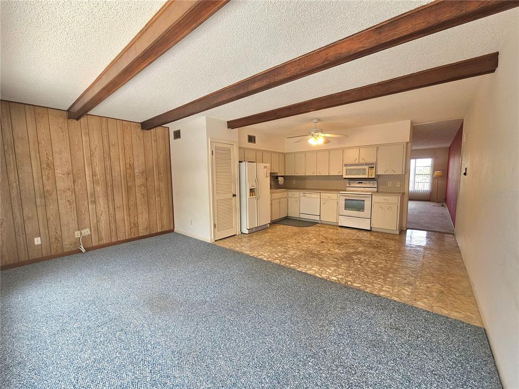 A living room with wood-paneled walls and exposed ceiling beams opens into a tiled kitchen — 2284 PHILIPPINE DRIVE UNIT 39, CLEARWATER, FL