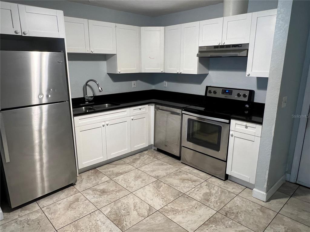 A kitchen features white cabinets, stainless steel appliances, black countertops, and light-colored tiled flooring — 920 MAYDELL DRIVE UNIT A, TAMPA, FL